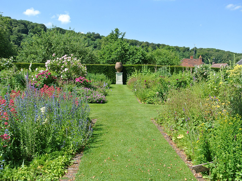 Landscaped six quarter's garden at Gilbert White's House with lush lawn and in bloom flowers