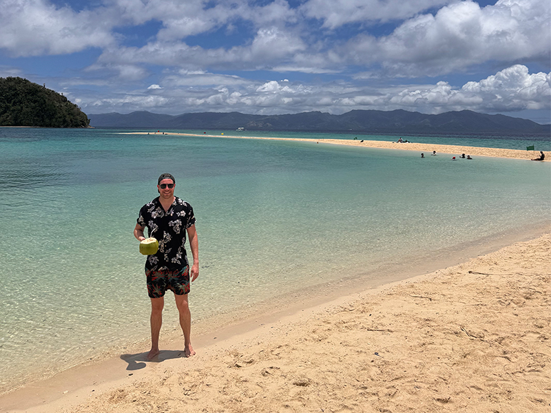 Charlie Mason standing on a beach in Raja Ampat holding a coconut